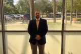 dave santos in professional attire standing in front of a window.