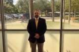 dave santos in professional attire standing in front of a window.