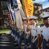 Norwich cadets stand in formation carrying flags and a rifle.