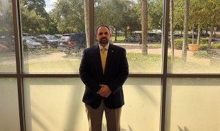 dave santos in professional attire standing in front of a window.