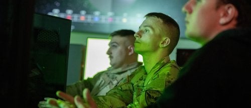 Three students in front of a computer in the Norwich University Cyber War Room.