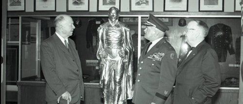 three men, one with cane, one in military uniform, gaze at a statue