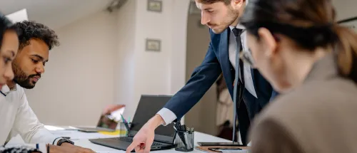 People review printed charts and documents around a conference table while one person points to a report.
