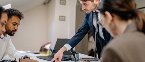 People review printed charts and documents around a conference table while one person points to a report.