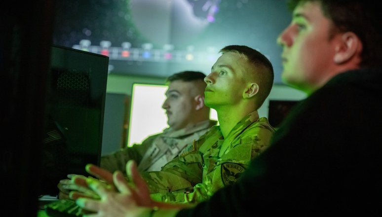 Three students in front of a computer in the Norwich University Cyber War Room.