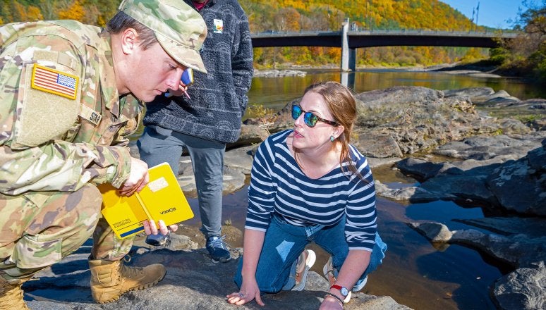 •	Instructor kneels on rocks beside a stream while a student examines the rock surface.